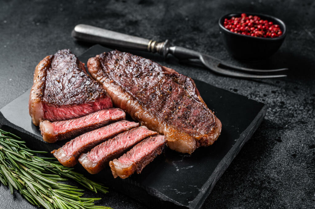 Grilled top sirloin or cup rump beef meat steak on marble board. Black background. Top view.