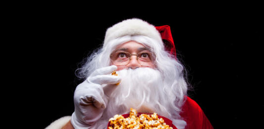 Christmas. Photo of Santa Claus gloved hand With a red bucket with popcorn, on a black background.