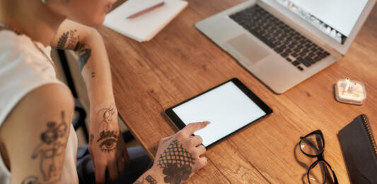 Young tattooed woman with short haircut using digital tablet while sitting at her workplace. Business woman at work. Cropped view. Workplace. Business concept