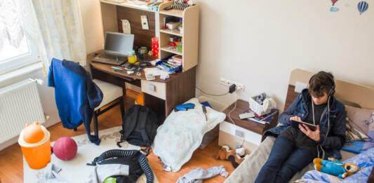 Teenager is using tablet in his messy room