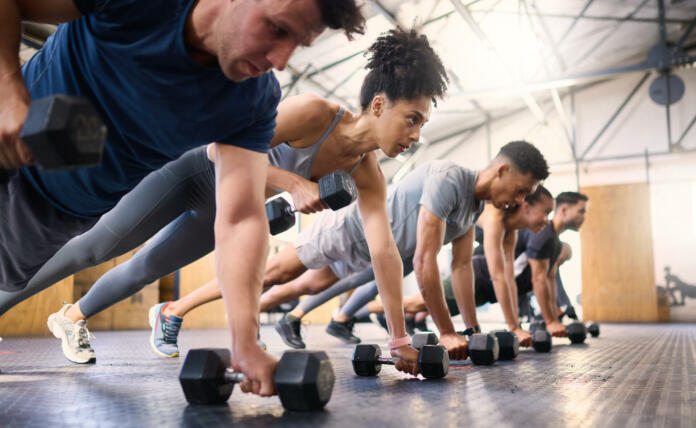 Strong, fitness and gym people with dumbbell teamwork training or exercise community, accountability and group. Sports diversity friends on floor in pushup muscle workout, power and wellness together