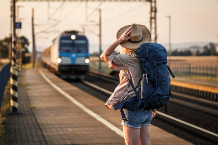 Woman backpacker with hat standing at railroad station and looking to arriving train