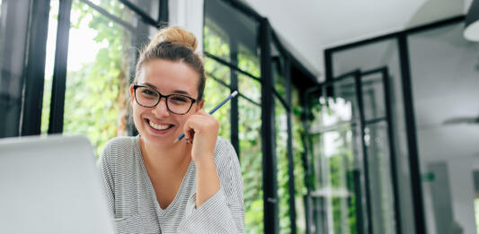 Portrait of smiling young female student in eyeglasses sitting in modern library.