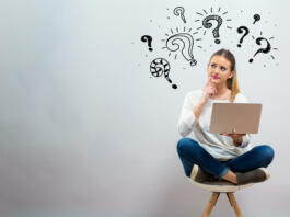 Question marks with young woman using her laptop on a grey background