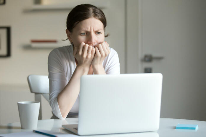 Portrait of a young woman at the desk with a laptop, her hands at her face at a fear. Business concept photo, lifestyle