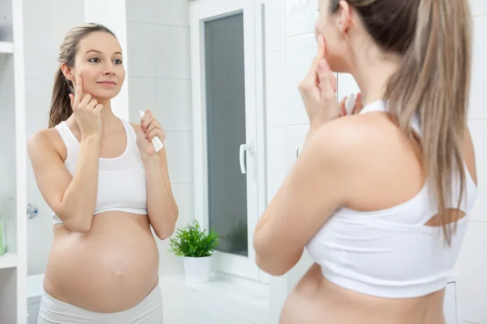 Pregnant woman in looking into bathroom mirror