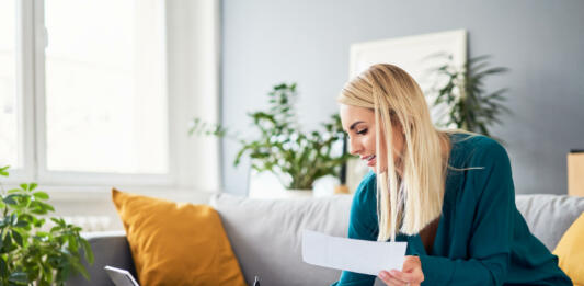 Smiling woman analysing bills filling tax documents while at sitting on sofa at home