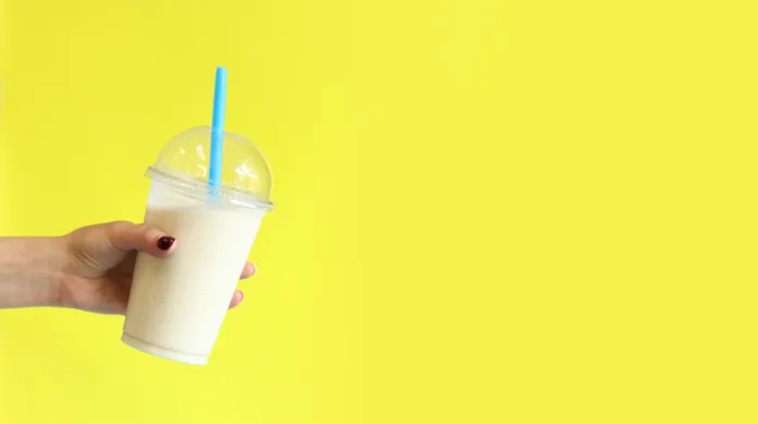 Banana smoothie with plastic disposable cup. Banana milkshake in a girl's hand on a bright yellow background. Copy space