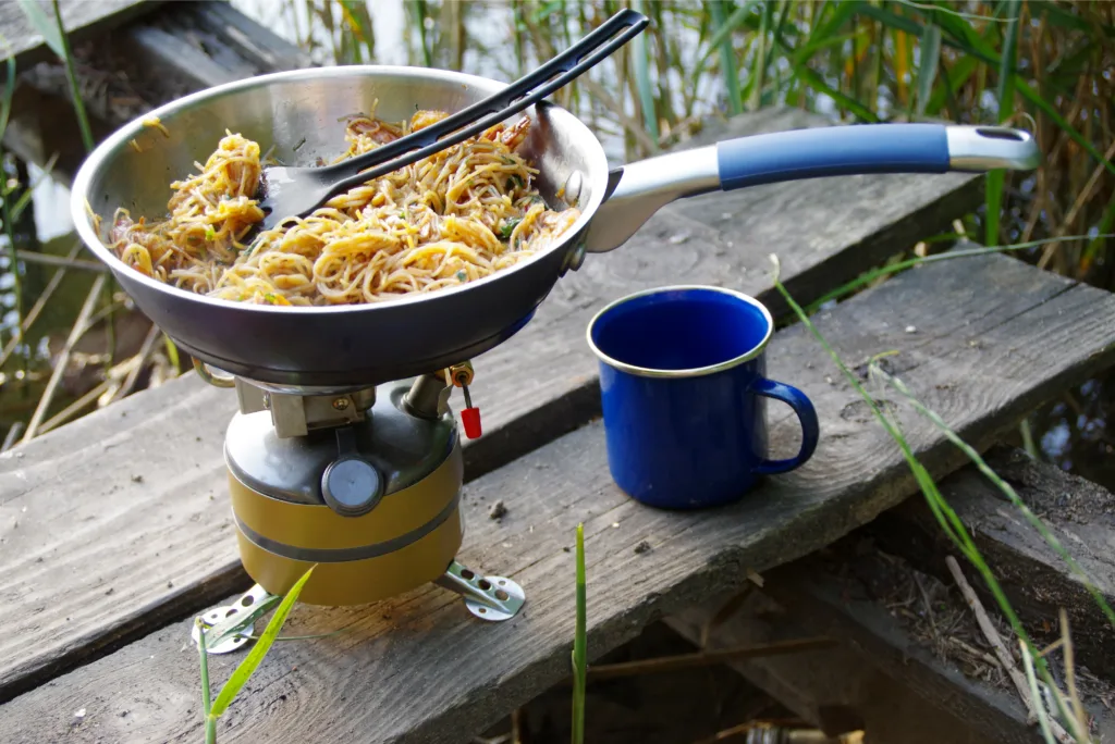 Camping food making. Pasta on pan on tourist fire stove. Camp cooking on the shore of the lake.