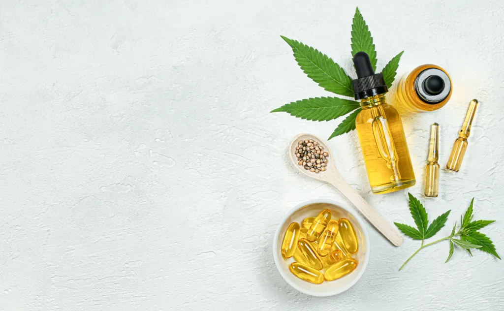 cbd oil, capsules, ampoules, seeds and fresh cannabis leaves on gray concrete background top view