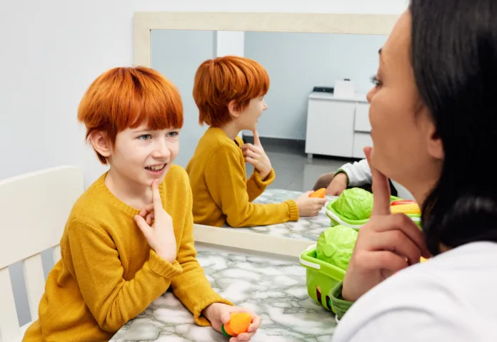 Female speech therapist working and training red-haired child with speech difficulties to develop speech, language and communication skills