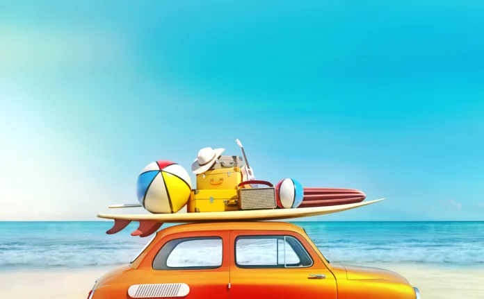 Small retro car with baggage, luggage and beach equipment on the roof, fully packed, ready for summer vacation, concept of a road trip with family and friends, dream destination, very vivid colors with dominant blue sky and ocean and bright orange car.