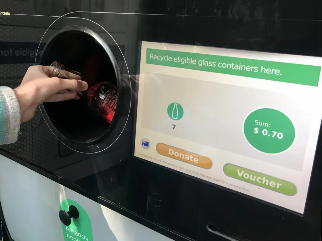 Sydney, Australia 08-16-2019. Return and Earn public return point for recycling. Reverse Vending Machine for refund and recycling of glass bottles. Hand holding a bottle
