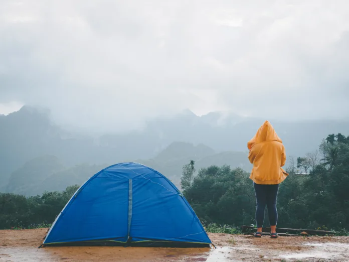 Woman camping blue tent on mountain peak and enjoying beautiful nature of hills and during rainy season at Doi Tapang, Sawi District, Chumphon, Thailand.