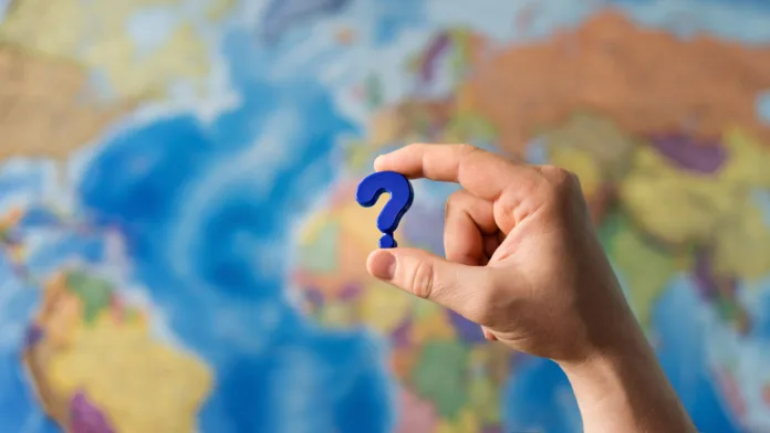 Adult hand holding question mark plastic toy on the world political map background. Travel planning explore destination concept. Quarantine over, borders open