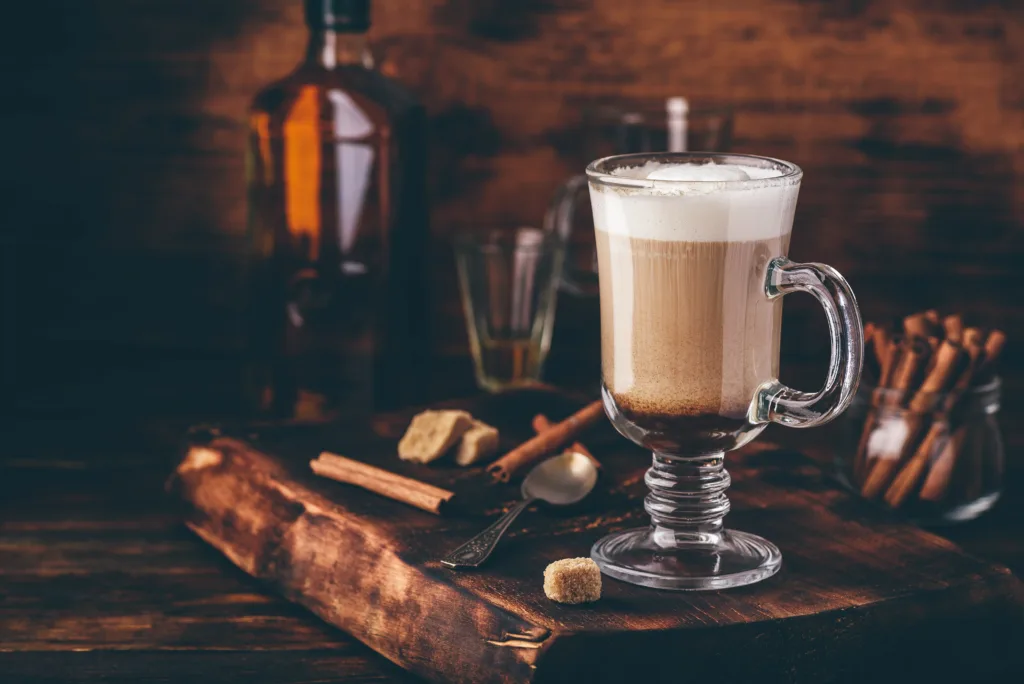 Coffee with Irish whiskey and whipped cream in glass on rustic wooden surface