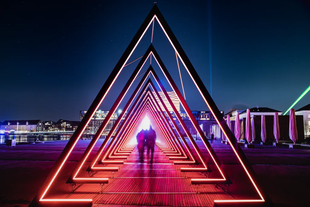 Copenhagen, Denmark - 19 February, 2020The light tunnel or gate of light installation consists of many triangular gates lit by bright lights, which should resemble a human trachea. Blurred people look like aliens crossing a deep light tunnel as stars are visible in the dark sky