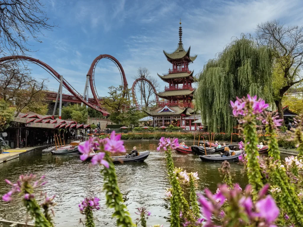 Copenhagen, Denmark - Oct 21, 2018: Pan-Asian Restaurant pagoda with The Demon (Daemonen) roller-coaster to left. People enjoying boating in artificial lake (foreground) in the Tivoli Gardens.