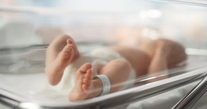 Cute Little Caucasian Newborn Baby Lying in Bassinet in a Maternity Hospital. Portrait of a Tiny Playful and Energetic Child with a Name ID Tag on the Leg. Healthcare, Pregnancy and Motherhood Concept