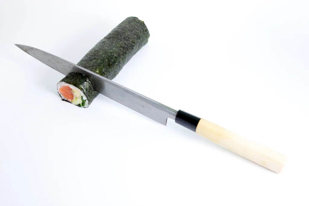 Cutting with a japanese knive a home-made futomaki of salmon, avocado, banana and courgette.