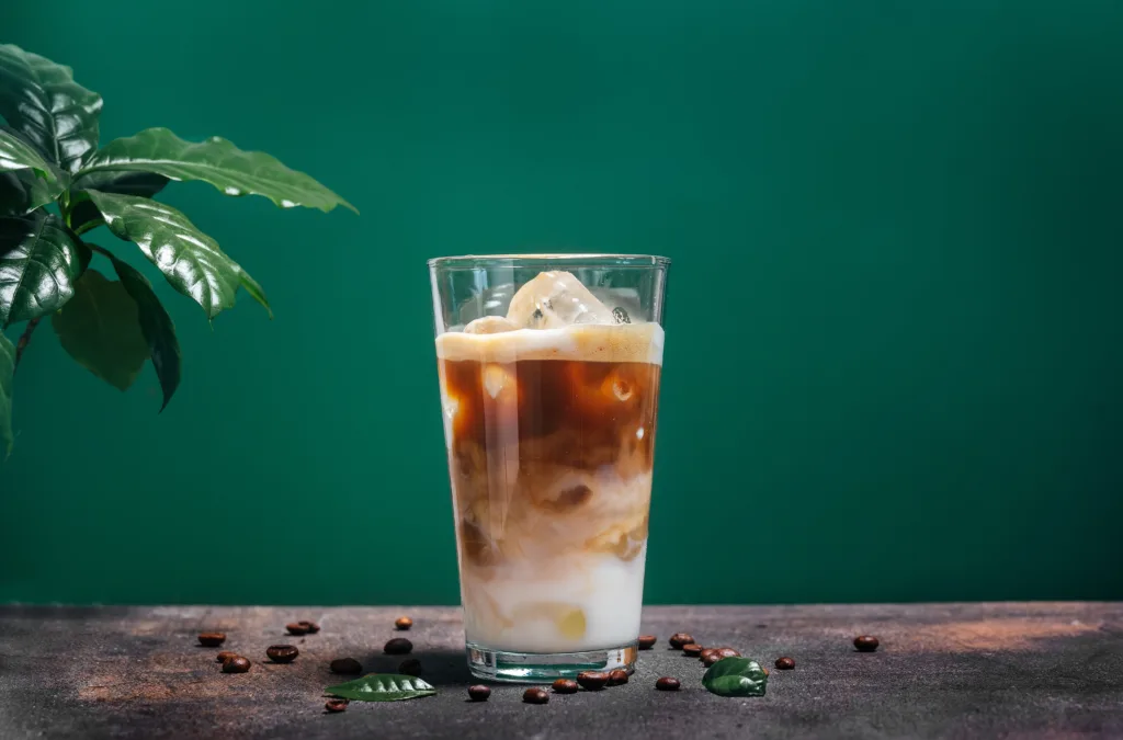 Delicious iced coffee latte in a glass on a green background with green leaves