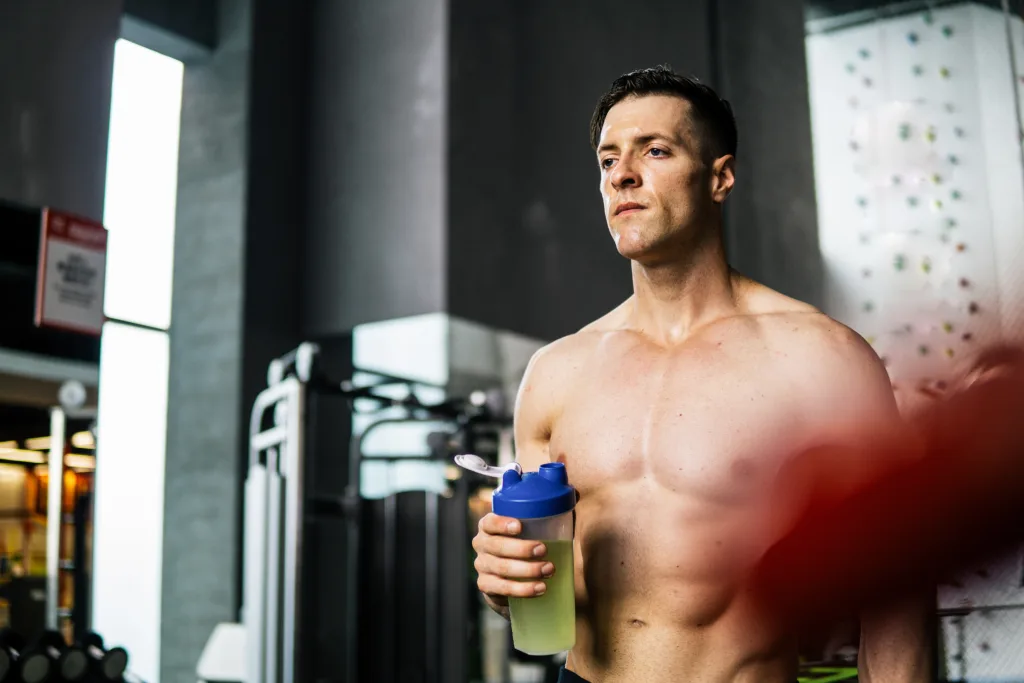 Handsome muscular male in gym, drinking protein shake