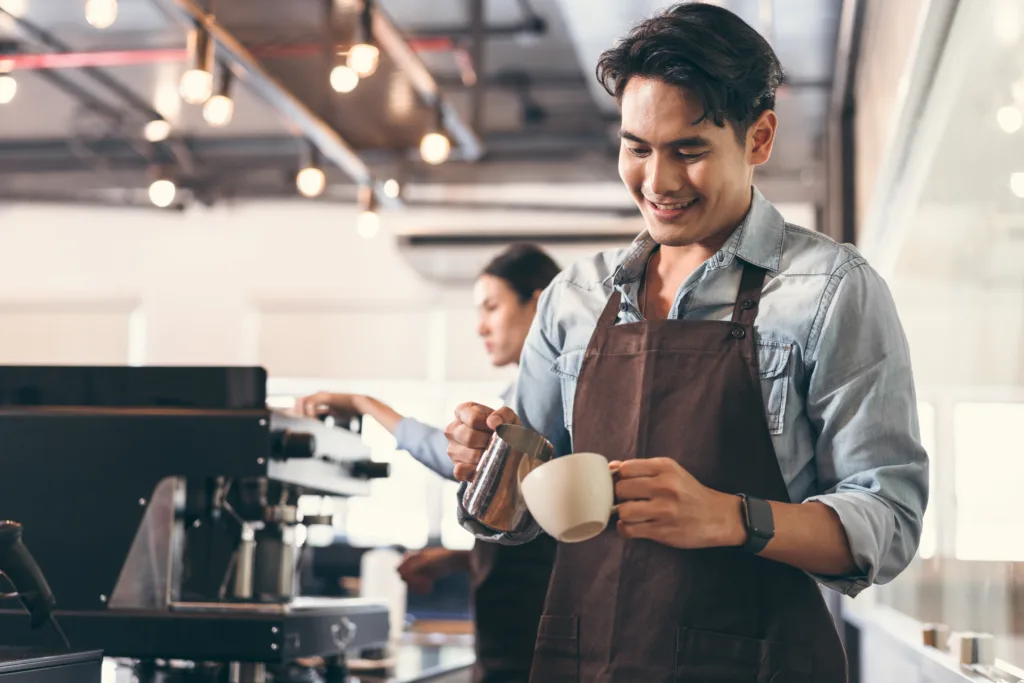 Happy barista Asia man make coffee with team work background at coffee shop