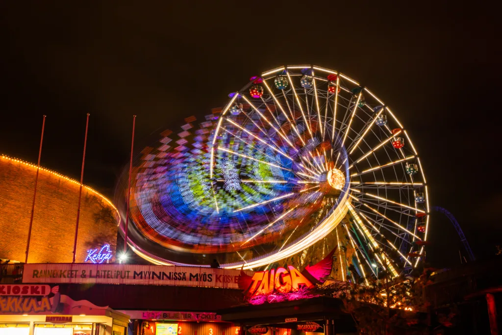 Helsinki, Finland - 19 October 2019: The Carnival of Light event at the Linnanmaki amusement park. Ride Ferris Wheel Rinkeli and Kehra in motion, night illumination, long exposure.