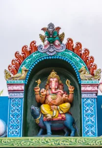 Kadirampura, Karnataka, India - November 4, 2013: Sri Murugan Temple. Colorful statue of green-red-blue niche with Ganesha sitting on his rat vehicle under silver sky. Monster mask on top.