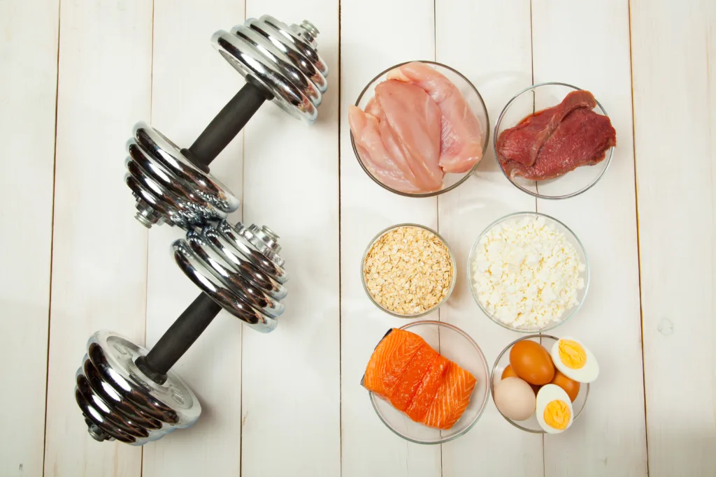 Protein diet, fish, cheese, eggs, meat, chicken and dumbbells on a white wooden background