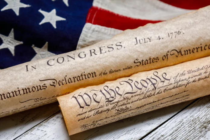 Rolled up copies of the US Constitution and Declaration of Independence with a vintage American flag on white painted weathered wood