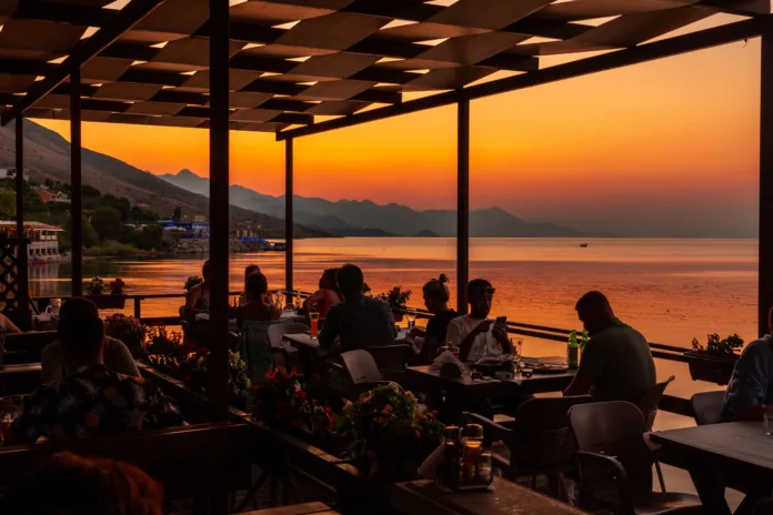 Tourists dining at beautiful orange summer sunset at Shkoder Lake in Shiroka Municipality. Albania