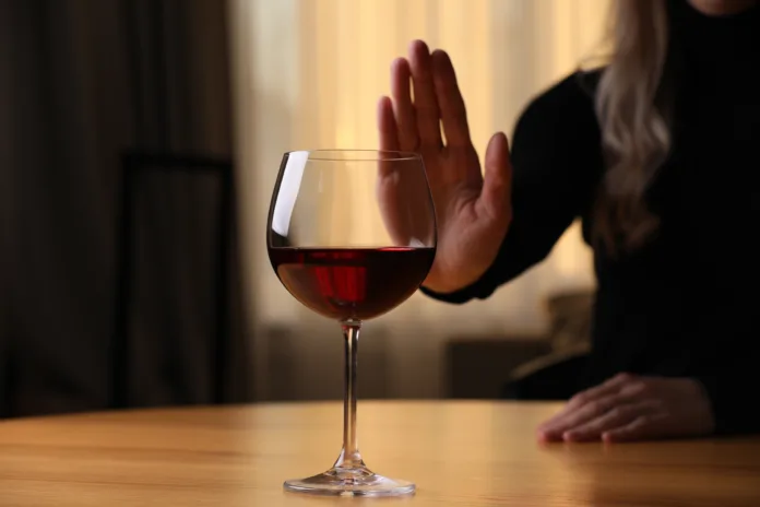 Woman refusing to drink red wine at home, closeup. Alcohol addiction treatment