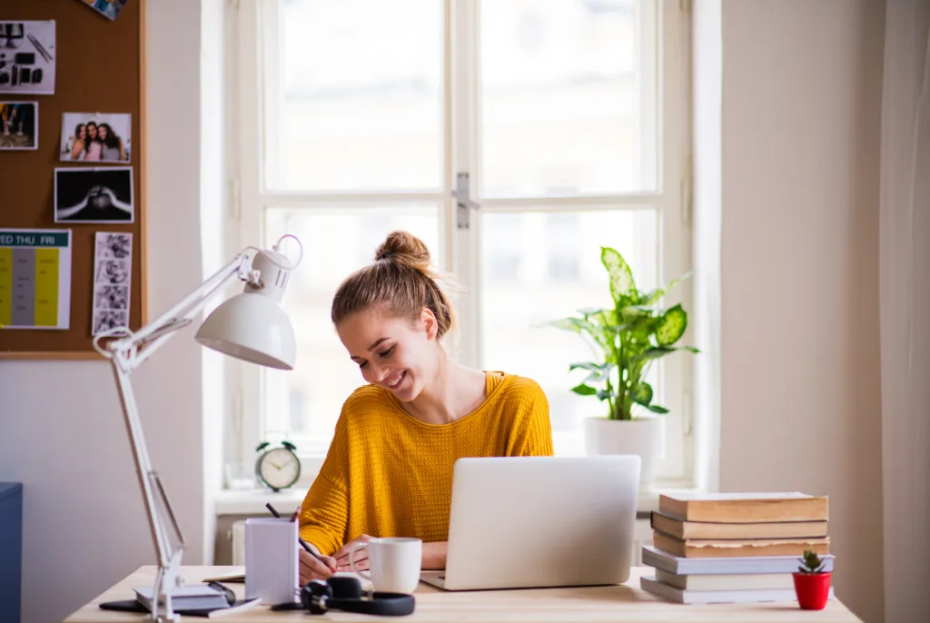 A young happy college female student sitting at the table at home, studying.