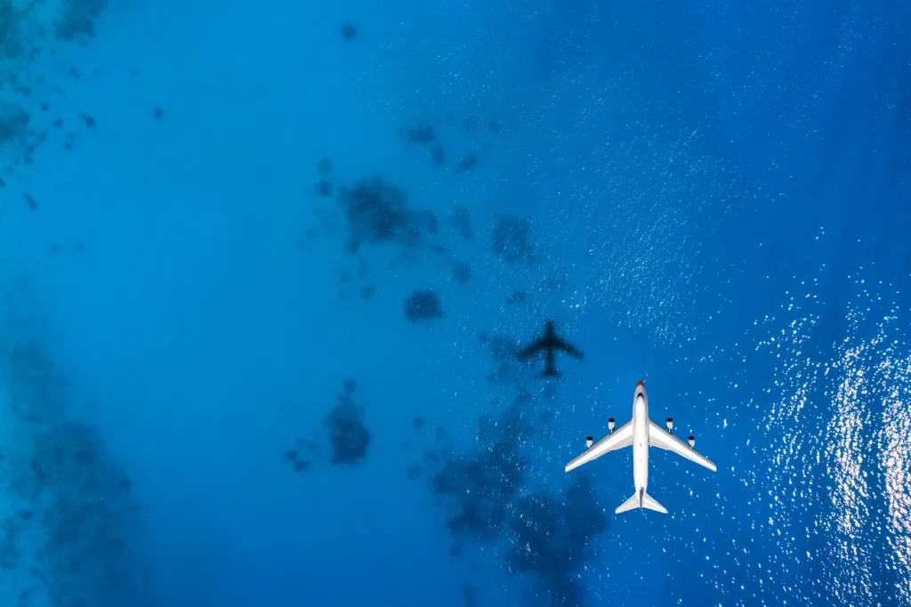 Aerial top down view of an airplane flying over blue sea as a travel concept with copy space