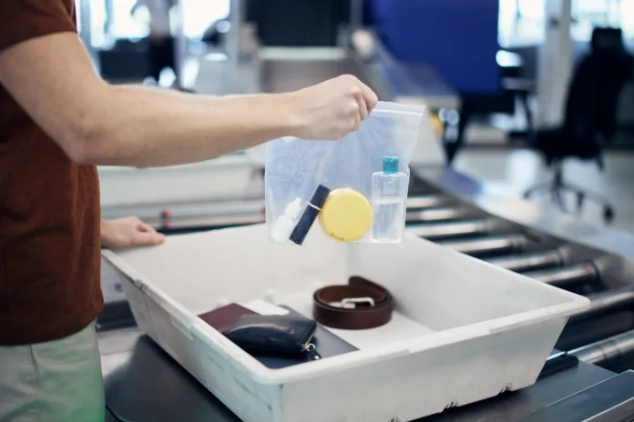 Airport security check before flight. Passenger holding plastic bag with liquids above container with laptop and personal items.