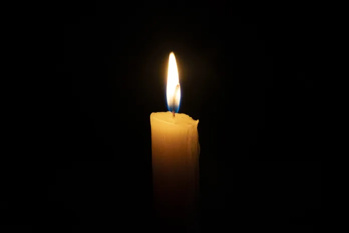 an orange candle burns in the dark on a black background. The concept of memory and sorrow.