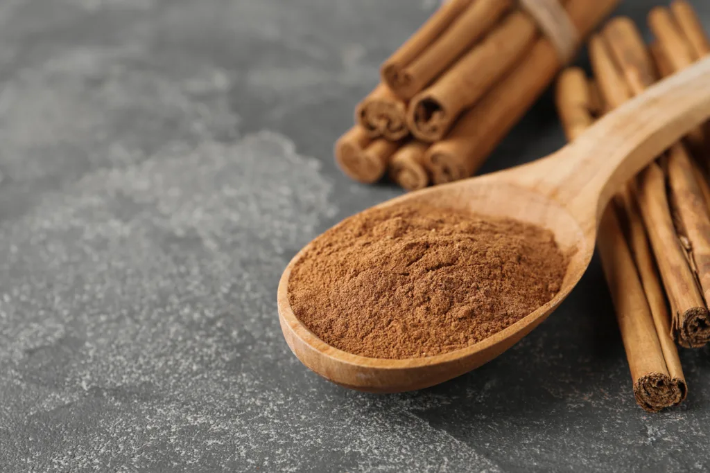 Aromatic cinnamon powder and sticks on grey table, closeup. Space for text