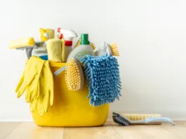 Brushes, bottles with cleaning liquids, sponges, rag and yellow rubber gloves on white background. Cleaning supplies in the yellow bucket on the wooden floor. Cleaning company service advertisement