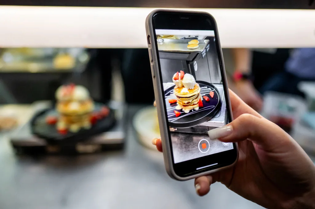 Close-up of a hand holding a smartphone, capturing a gourmet dessert in a restaurant setting