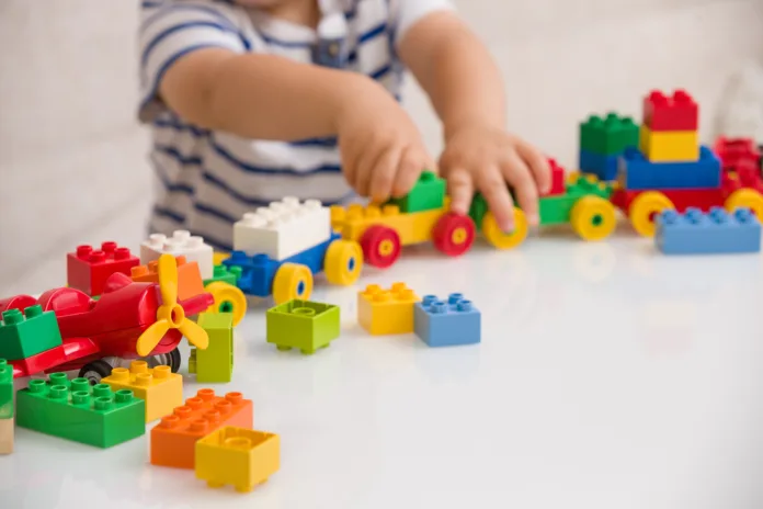 Close up of child's hands playing with colorful plastic bricks at the table. Toddler having fun and building out of bright constructor bricks. Early learning. stripe background. Developing toys