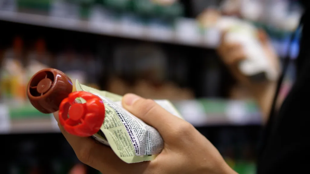 Closeup of a woman's hand. She is holding mashed potatoes. A woman reads the ingredients on a package. Selection of baby food with different flavors in the grocery super market.