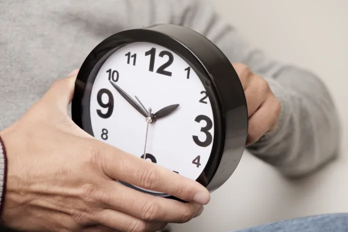 closeup of a young caucasian man adjusting the time of a clock