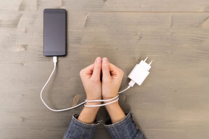 Female hands and smartphone. Woman's hands trapped and wrapped on wrists with mobile phone cable as handcuffs. Addiction to internet and social networks