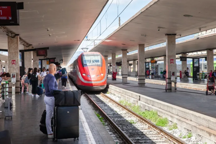 FLORENCE, ITALY - JUNE 15, 2024: Picture of a frecciarossa train entering Florence train station. Frecciarossa is a high-speed train of the Italian national train operator, Trenitalia, as well as a member of the train category Le Frecce. The name was introduced in 2008 after it had previously been known as Eurostar Italia. This photograph captures the arrival of a Frecciarossa train from Trenitalia at the Firenze Santa Maria Novella station. The sleek, modern design of the train highlights the advanced technology and efficiency of Italy's high-speed rail system. Passengers are seen waiting on the platform, ready to embark on their journey, showcasing the importance of rail travel in connecting cities across Italy. The image reflects the dynamic and fast-paced nature of transportation in one of Italy's major transit hubs.