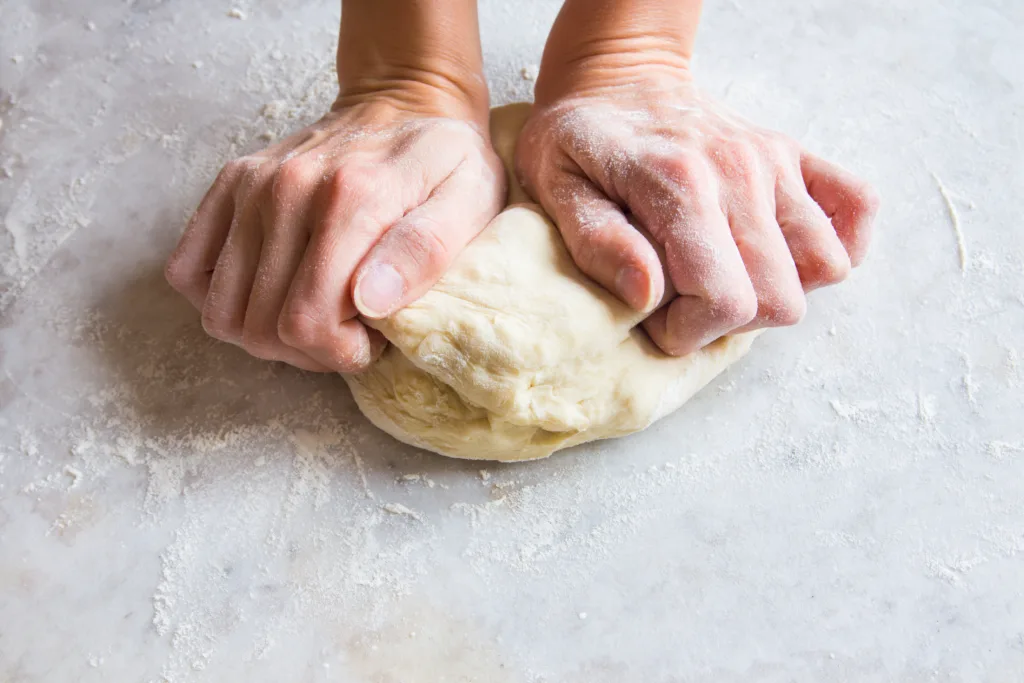 Hands knead dough on cutting board for homemade bakery