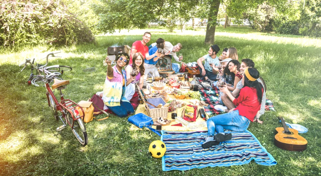 Happy friends group having fun outdoor cheering at bbq picnic with snacks food drinking red wine - Young people enjoying spring time together at barbecue garden party - Youth milennials concept