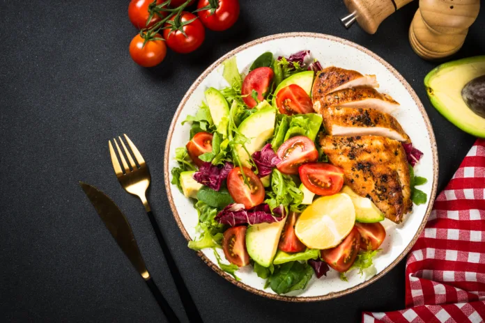 Healthy salad with leaves, vegetables andGrilled chicken steak. Top view at black table.