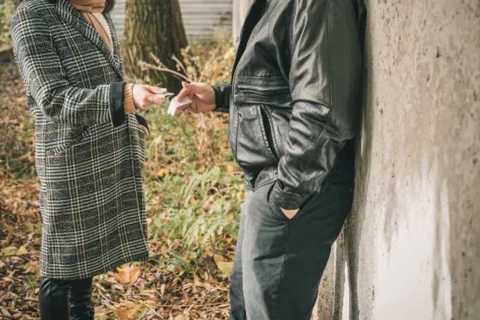 Male drug dealer sells hard drugs in a transparent plastic bag to an addicted woman with money in her hand, cropped image.