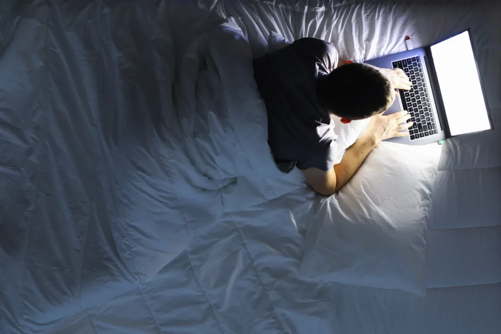 Man in bed with laptop using internet in online service love chat closeup background. Round the clock helpline concept